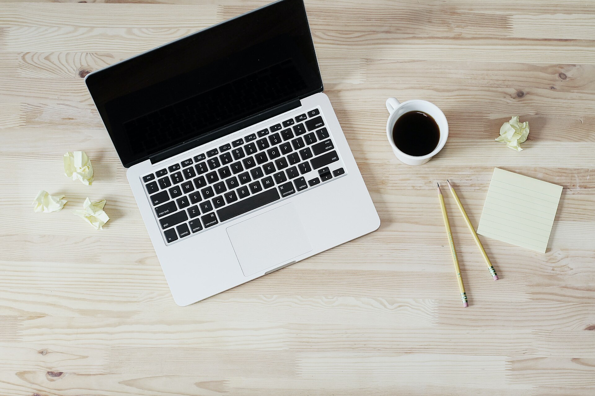 Ordinateur portable éteint, tasse de café, crayons et bloc-notes sur un bureau en bois clair